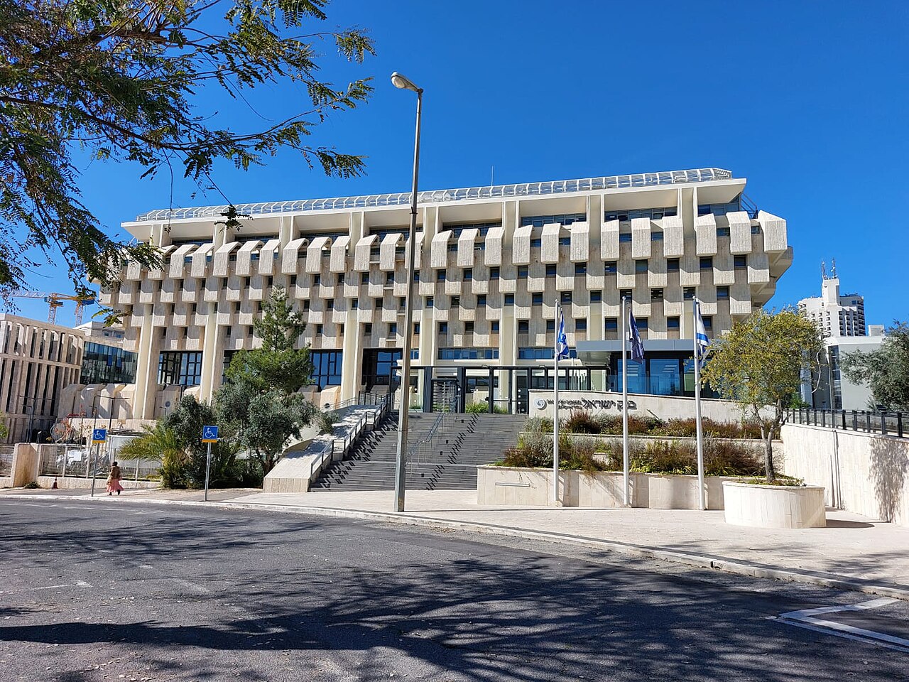 מבנה גדול ומיוחד בסגנון מודרני, עם חלונות רבים, קומות בולטות ומדרגות רחבות, מוקף בעצים, שדרות דגלים, ורחוב סלול.