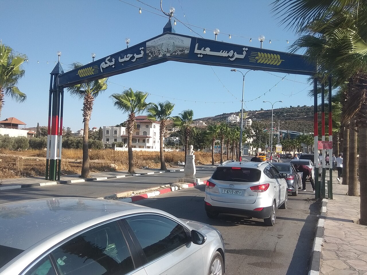 תמונת חדשות: תמונה של כביש עם שער מעליו וכתב זר עליו. טקסט חלופי: תמונה של כביש עם שער כחול מעליו, ועליו כתב בערבית ודגניים צהובים.