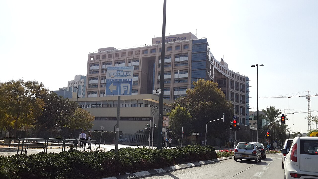 בניין רב קומות לצד כביש עם כלי רכב נוסעים בו, ועל הבניין שלט גדול.