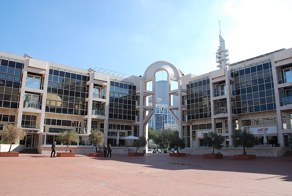 מבנה ציבור גדול ומודרני, עם חלונות רבים, עמודים גבוהים, ורחבה עם עצים.