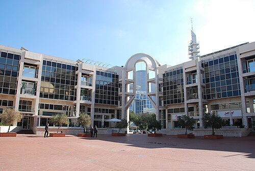 מבנה ציבור גדול ומודרני, עם חלונות רבים, עמודים גבוהים, ורחבה עם עצים.